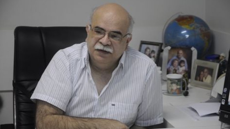 Foto do professor Manuel Cardoso, sentado junto a uma mesa com objetos pessoais e de trabalho