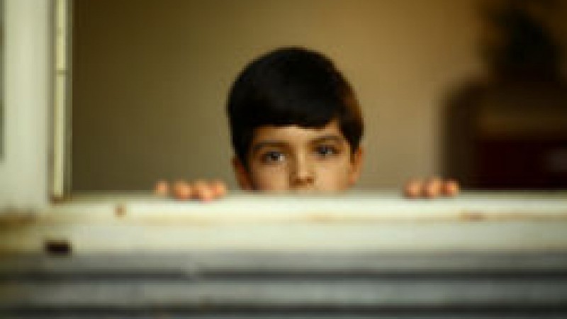 Imagem de O Filho do Vizinho, um menino com o rosto olhando para fora da janela.