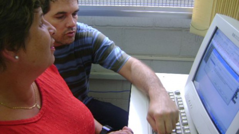 Senhora com deficiência visual utilizando o computador ao lado de instrutor.