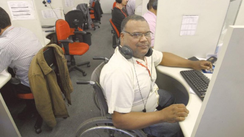 Ronaldo Goulart deixou de trabalhar em várias empresas em BH por que elas não estavam adaptadas. Descrição da imagem: Sala de tele-marketing com cabines separadas e vários consultores de venda sentados ao fundo com fones de ouvido, e o consultor Ronaldo