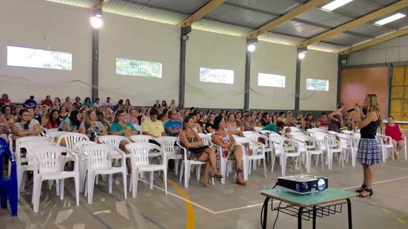 Descrição da imagem: Palestra Mirelle de pé com microfone na mão e ao fundo o público sentado em fileiras em cadeiras brancas. Crédito da foto: Divulgação