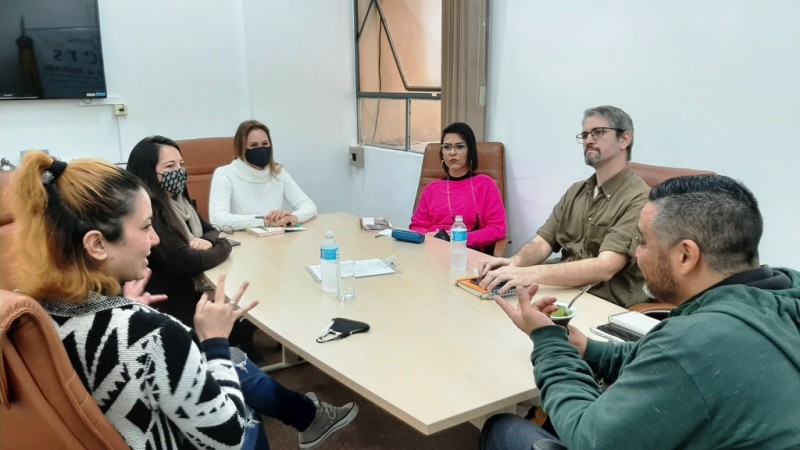 Seis pessoas estão sentados ao redor de uma mesa, sendo quatro mulheres e dois homens.