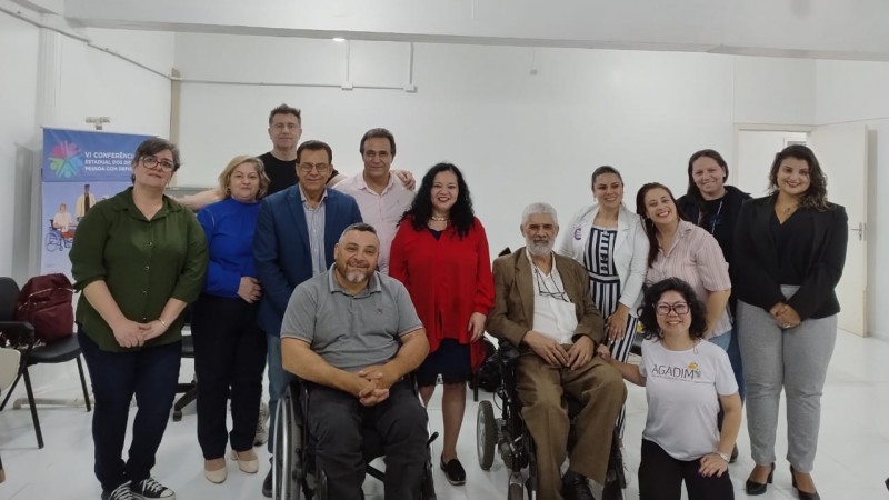 Foto: em suas cadeiras de rodas os presidentes da Faders e do Coepede, em pé os participantes da inauguração da nova sede do Conselho que aconteceu neste dia 01 pela manhã e fica no predio da Faders na Morretes. Ao fundo paredes brancas, teto branco, e piso branco. Fim da descrição