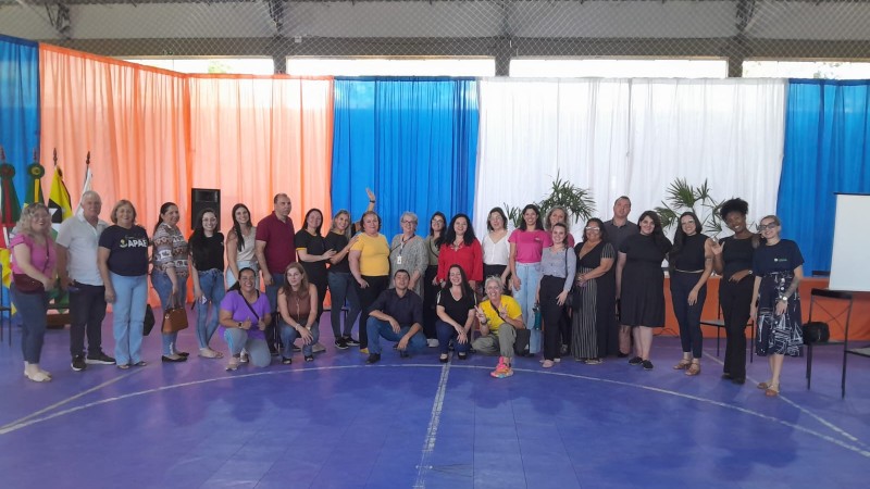 Foto com todos os participantes do fórum, alguns em pés e outros em frente abaixados. o chão é azul, e ao fundo cortinas em azul branco e laranja. Fim da Descrição