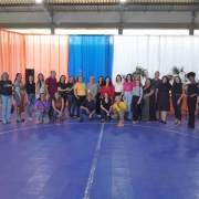 Foto com todos os participantes do fórum, alguns em pés e outros em frente abaixados. o chão é azul, e ao fundo cortinas em azul branco e laranja. Fim da Descrição