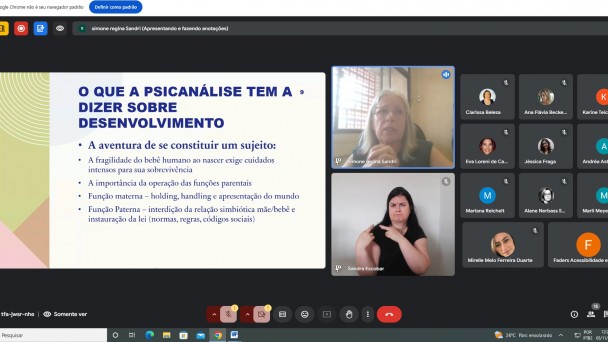 Foto da tela do computador - no canto esquerdo aparece as laminas que estão sendo apresentadas na aula de Constituição Psíquica, ao lado em formato grande a imagem da professora que explica o conteúdo e abaixo da intérprete de libras, ao lado na direita- em ícones menores as janelas dos participantes do curso. Fim da descrição 