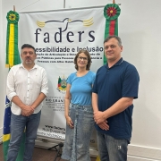 foto - no fundo parede branca, a frente um banner da Faders onde aos lados estão , no esquerdo a bandeira do Brasil e na direita a bandeira do RS, em frente e em pé da esquerda para a direita está o secretário de Trabalho de Marau, a coordenadora de Capacitação e o chefe de gabinete da Faders