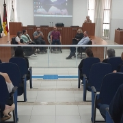 Foto: aparecem cadeiras azuis onde está o publico do evento, e na frente há uma separação em vidro, e então a mesa em formato de U em madeira, no fundo uma mesa mais alta ( inde fica a mesa diretora da Cãmara em dias de sessão) e há o pulpito, onde se pronuncia uma senhora loira de cabelos curtos e que veste bege. na Frente estão sentados os palestrantes em cadeiras pretas e o presidente da Faders em sua cadeira de rodas; Fim da descrição 