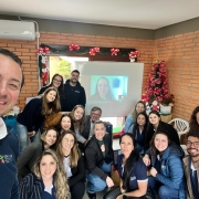 Foto- selfie, as paredes são em tijolo a vista, no fundo um painel onde aparece a coordenadora de Pesquisa da Faders On Line, e ao redor, uns em pé e uns abaixados, os profissionais que participaram da capacitação sobre Autismo e a Ciptea. Bem na frente quem fez a selfie é um homem claro, com cabelos curots castanhos, olho claro, e com uma blusa azul. Fim da Descrição