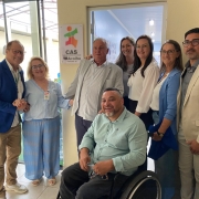 Foto das autoridades presentes na inauguração em frente a uma das portas que abriga o espaço do CAS Teacolhe junto a Apae. No centro o Presidente da Faders. Fim da Descrição