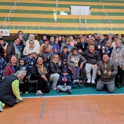 Foto- no estádio Militão, ao fundo aparecem as arquibancadas em verde e amarelo, na quadra já está o grupo que participou do Desafie-se Faders alguns em pés e uns  no chão sentados ou acocorados. Todos com suas medalhas de participação, muito sorridentes, entre eles além dos alunos, professores, familiares e equipe de Bagé da faders que organizou o  evento. No centro o presidente da Faders em sua cadeira de rodas e os representantes das instituições com maior número de participantes que tem em mãos o troféu recebido. Fim da descrição