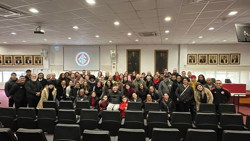 Foto - do auditório, ao fundo os quadros com as fotos dos ex-presidentes do Inter, em uma parede branca, no canto esquerdo em um telão a logo do Time. Na frente entre as cadeiras com encosto preto estão os participantes do curso, dirigentes e a equipe da Faders que conduziu a capacitação junto com o presidente da entidade. Fim da descrição