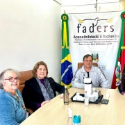 Foto - ao redor de uma mesa de tampa clara estao o chefe de gabinete da Faders, e a diretora técnica da faders, reunidos com as gestoras de NH, ao fundo o banner da Faders e as bandeiras do Brasil e do RS.