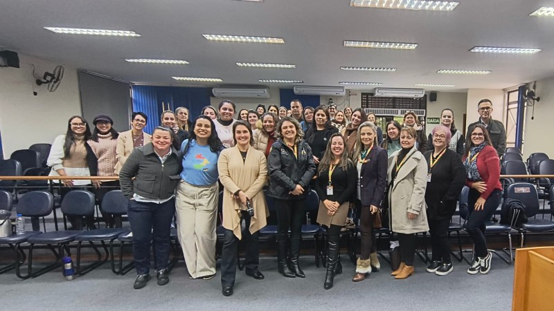 Foto ambiente interno, parece claras cortinas azuis, carpete cinza no ch&atilde;o, cadeiras pretas e em primeiro plano os participantes da oficina posam para foto com as ministrantes das atividades - servidoras da Faders 